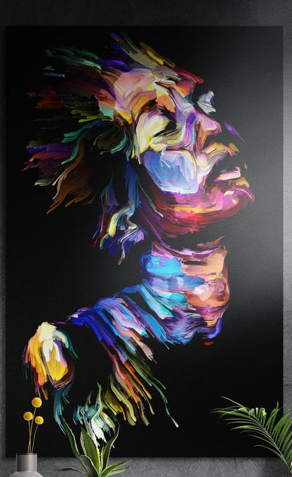 Rainbow brushstroke face in profile brushed aluminum wall art on a dark textured wall behind a vase and plants