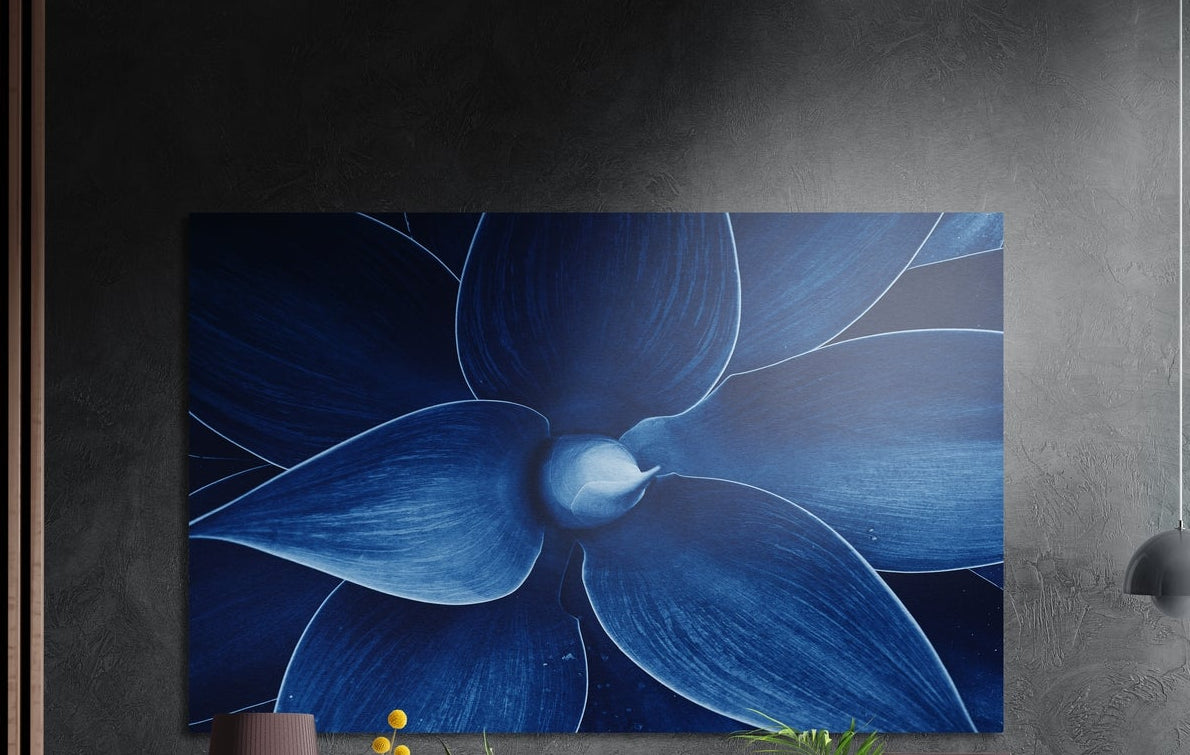 Deep blue flower petals macro brushed aluminum wall art on a dark textured wall above a lamp and yellow flowers