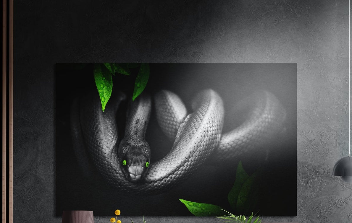 Coiled silver snake with green eyes and leaves brushed aluminum wall art on a dark gray wall above plants