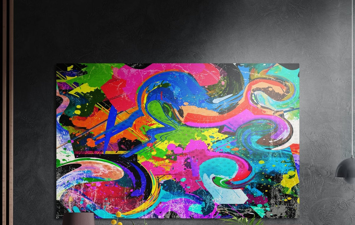Neon paint swirls and splatter abstract brushed aluminum wall art on a dark gray wall above yellow flowers