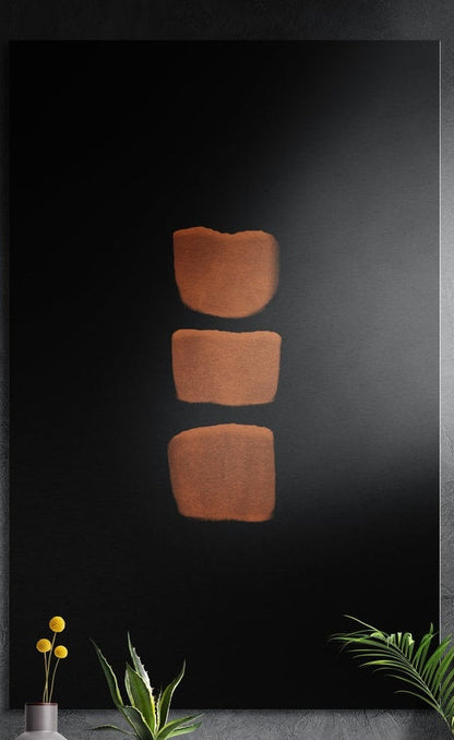 Three copper blocks stacked on black, brushed aluminum wall art on a dark gray wall above yellow flowers