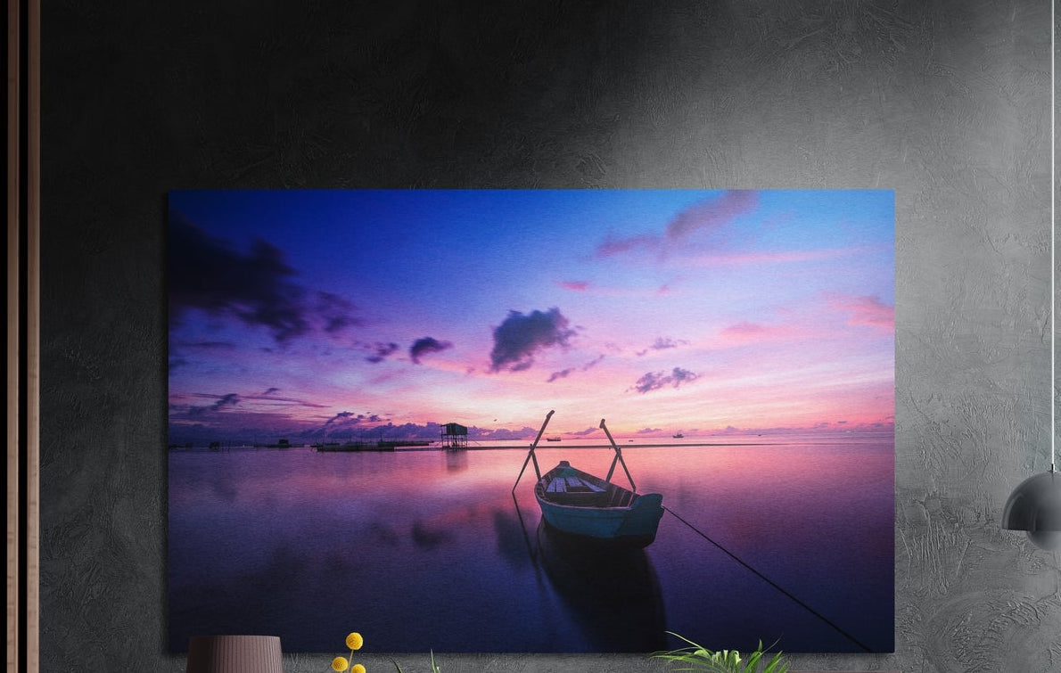 Lone boat on a purple lake brushed aluminum wall art on a dark gray wall above a sideboard with a vase and plants