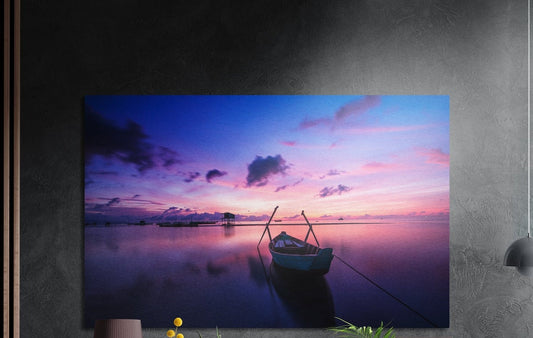 Lone boat on a purple lake brushed aluminum wall art on a dark gray wall above a sideboard with a vase and plants