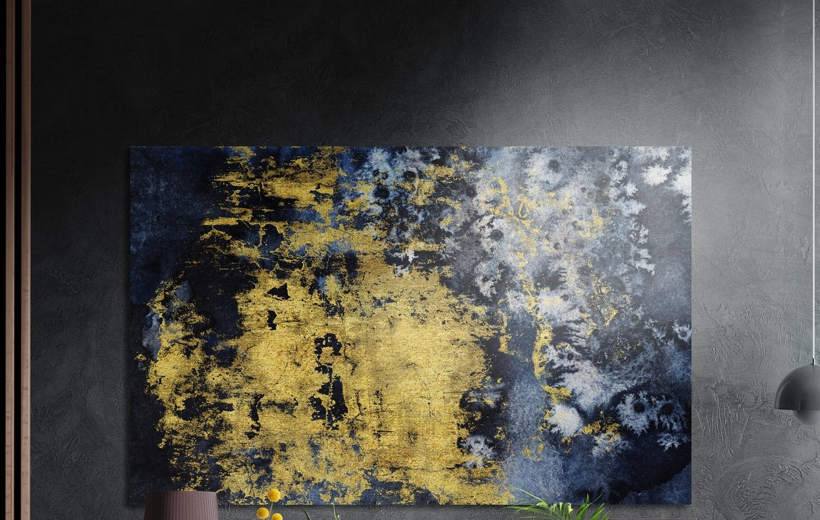 Gold and navy distressed abstract brushed aluminum wall art on a dark wall above a vase and plants