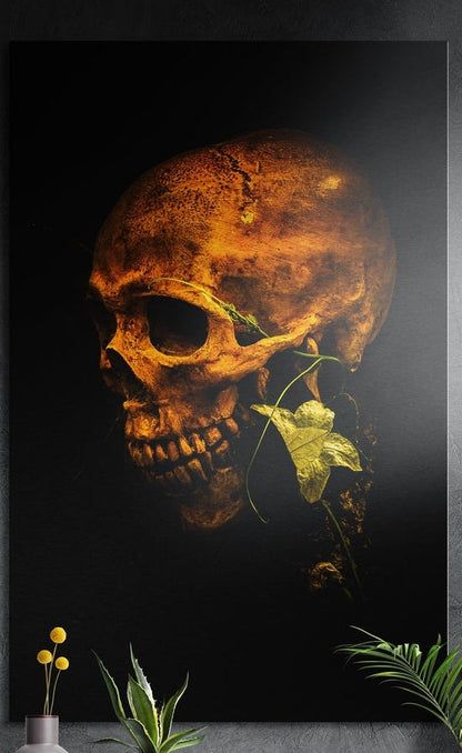 Golden skull with ivy leaf on black brushed aluminum wall art on a gray concrete wall above small plants