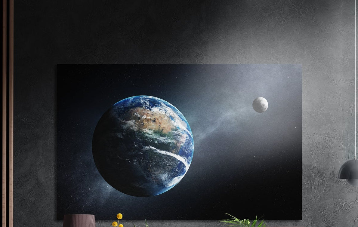 Earth and distant moon in space brushed aluminum wall art on a gray concrete wall with a lamp and plants below