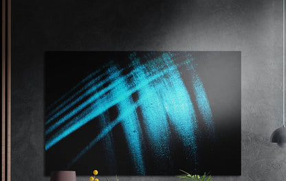Turquoise brushstroke on black brushed aluminum wall art on a dark textured wall with plants below