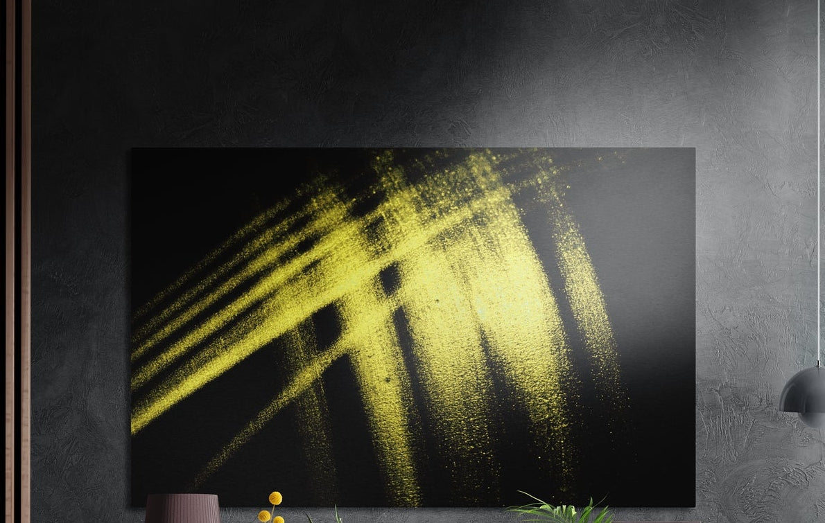 Yellow brushstroke on black brushed aluminum wall art on a dark textured wall with plants below