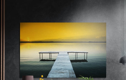 Wooden pier on a golden sunset lake, brushed aluminum wall art on a dark gray wall above a vase and yellow flowers