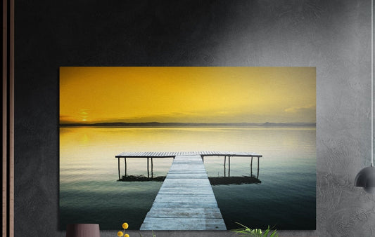 Wooden pier on a golden sunset lake, brushed aluminum wall art on a dark gray wall above a vase and yellow flowers