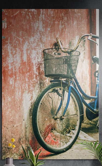 Blue bicycle against a peeling red wall, brushed aluminum wall art on a dark gray wall above yellow flowers