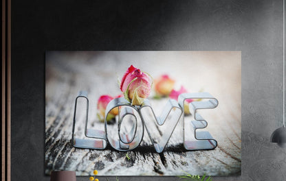 Silver love cookie cutter letters with pink rosebuds on weathered wood, brushed aluminum wall art on a dark wall