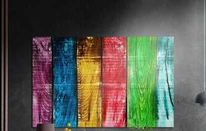 Rainbow wood plank brushed aluminum wall art on a dark textured wall above a lamp and yellow flowers