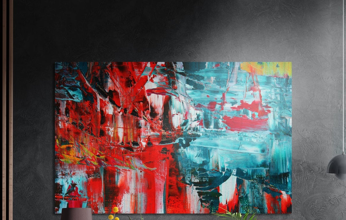 Red and turquoise brushstroke abstract brushed aluminum wall art on a dark wall above a vase and plants