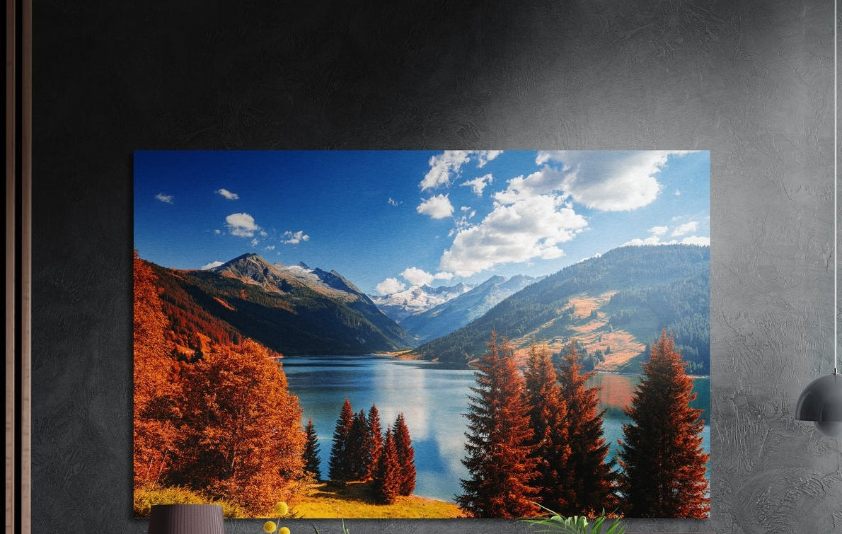 Alpine lake with red pines brushed aluminum wall art on a dark gray wall above a sideboard with a vase and plants