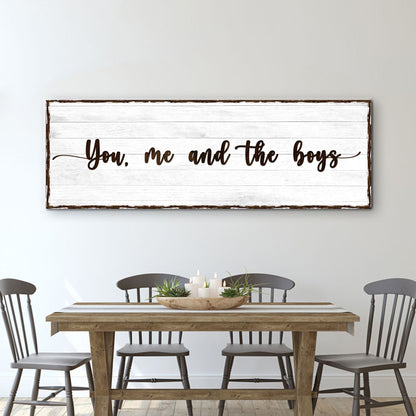Wide canvas sign with a white wood plank look and brown script reading You, me and the boys, above a dining table