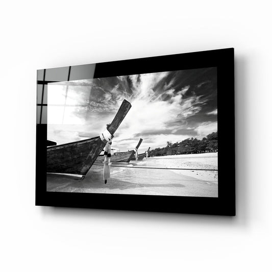 Black and white longtail boat glass wall art with wooden boats beached under streaked clouds