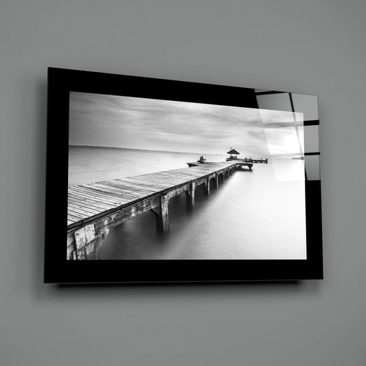 Black and white long pier and gazebo glass wall art with a black border hung on a plain gray wall
