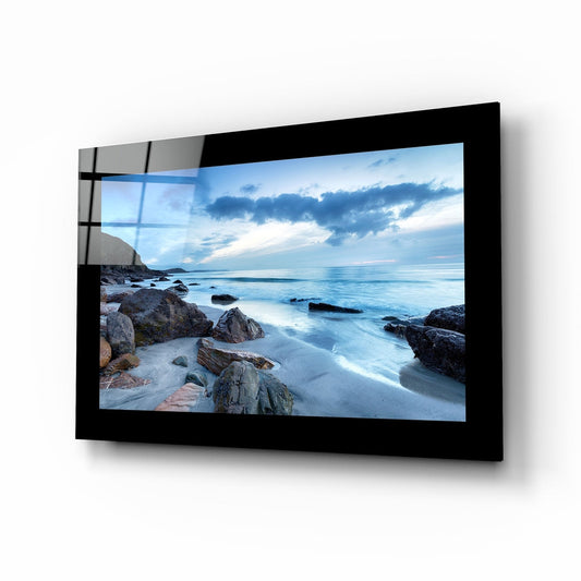 Coast glass wall art with boulders on pale sand beside a calm blue cove