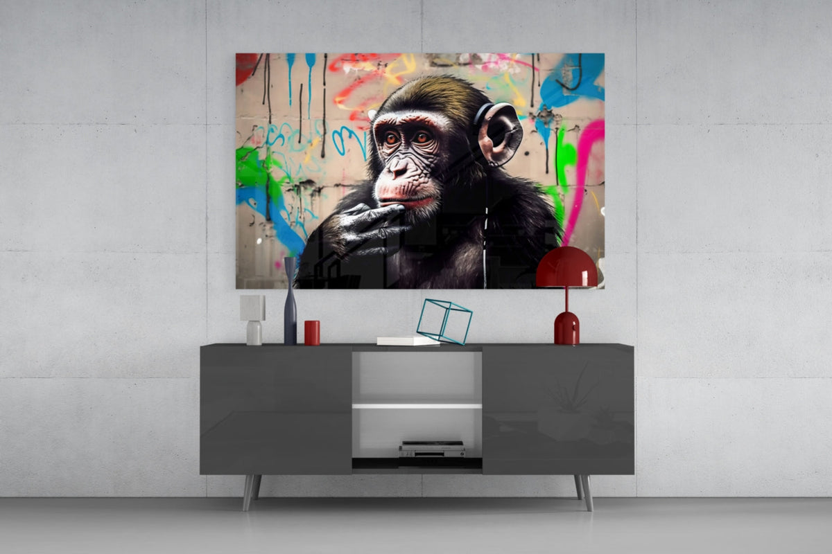 Thinking chimpanzee with headphones glass wall art above a gray sideboard with a red table lamp