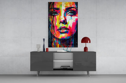 Rainbow paint drip woman face glass wall art above a gray sideboard with a red lamp on a concrete wall
