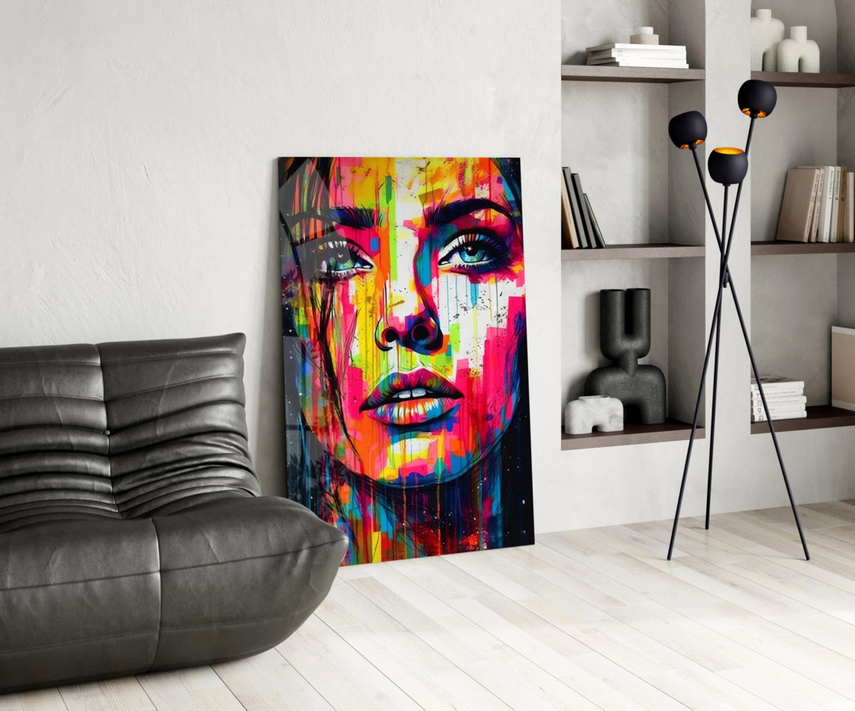 Rainbow paint drip woman face glass wall art leaning beside a black leather lounge chair and shelves