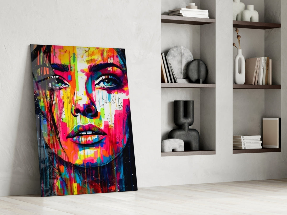 Rainbow paint drip woman face glass wall art leaning against a white wall beside built-in shelves