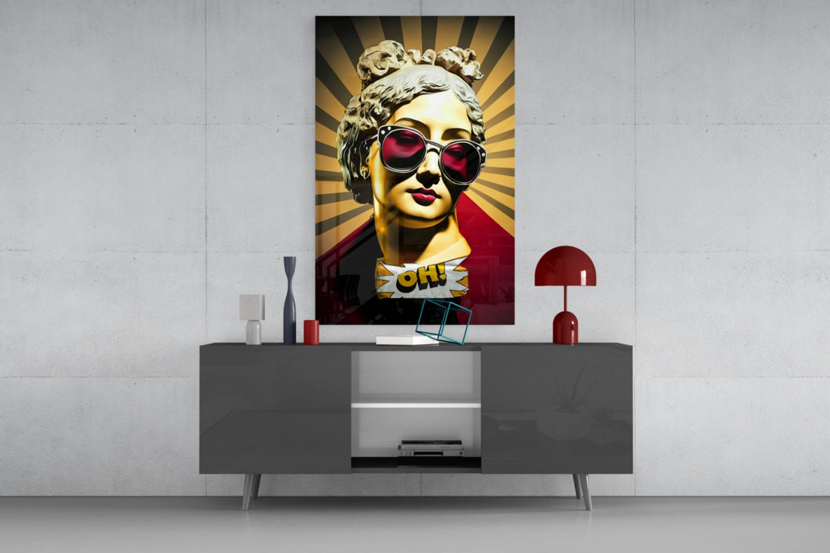Gold bust in sunglasses on sunburst rays glass wall art above a gray sideboard with a red table lamp on a concrete wall