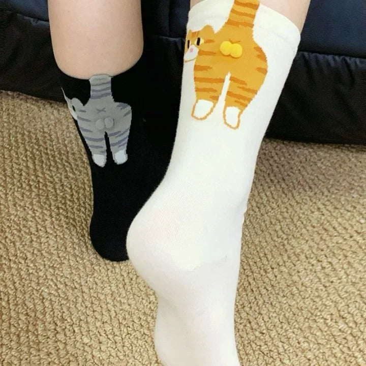 White socks with cat design worn by a person on a carpeted floor.