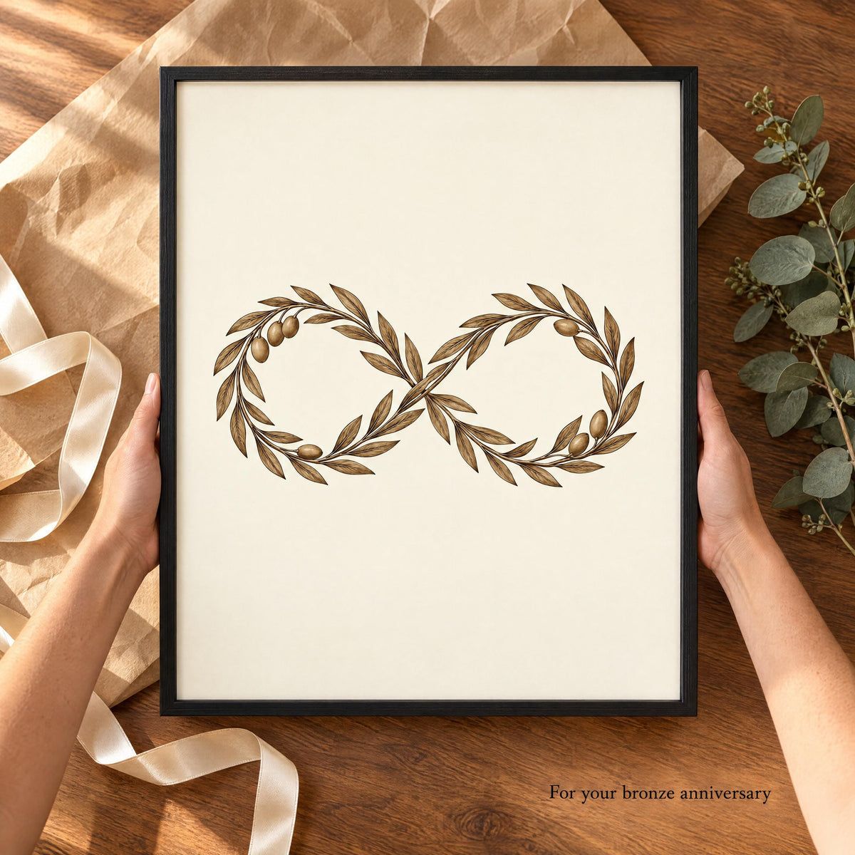 Hands holding the framed olive infinity print over kraft paper and ribbon, captioned For your bronze anniversary