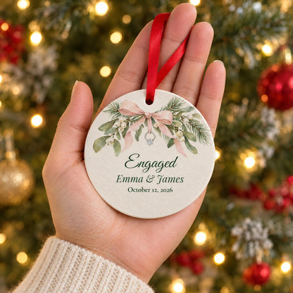 Palm-size engaged couple ornament held in an open hand in front of a lit Christmas tree