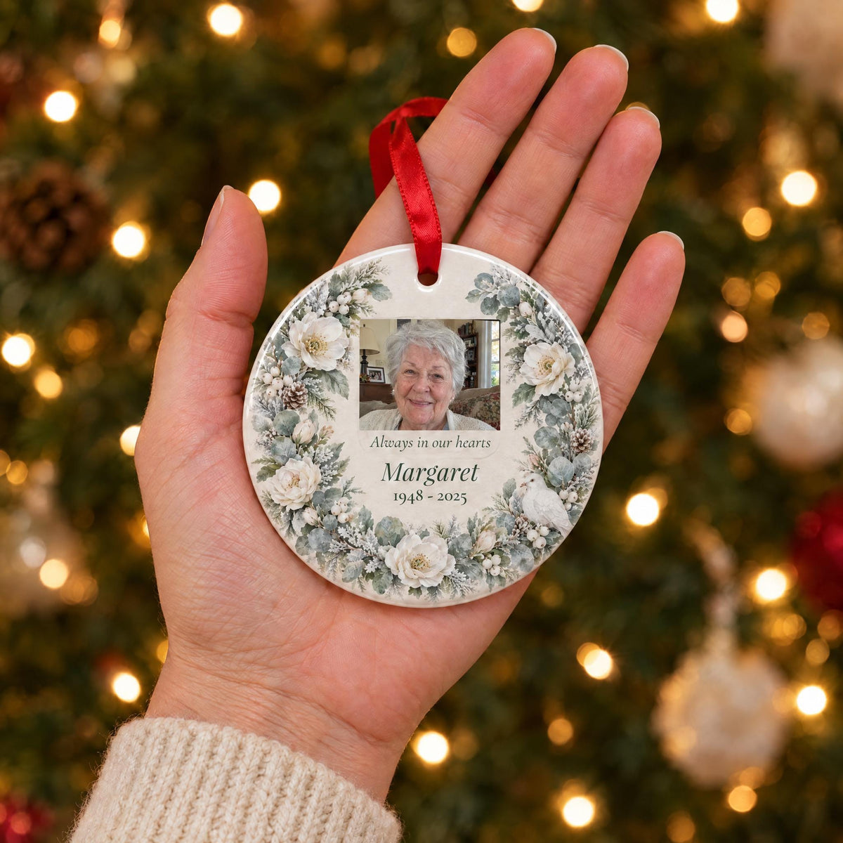 Palm-size memorial photo ornament held in an open hand in front of a lit Christmas tree