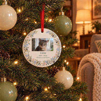 Cat memorial ornament with a tabby cat photo hanging on a lit Christmas tree in a cozy living room