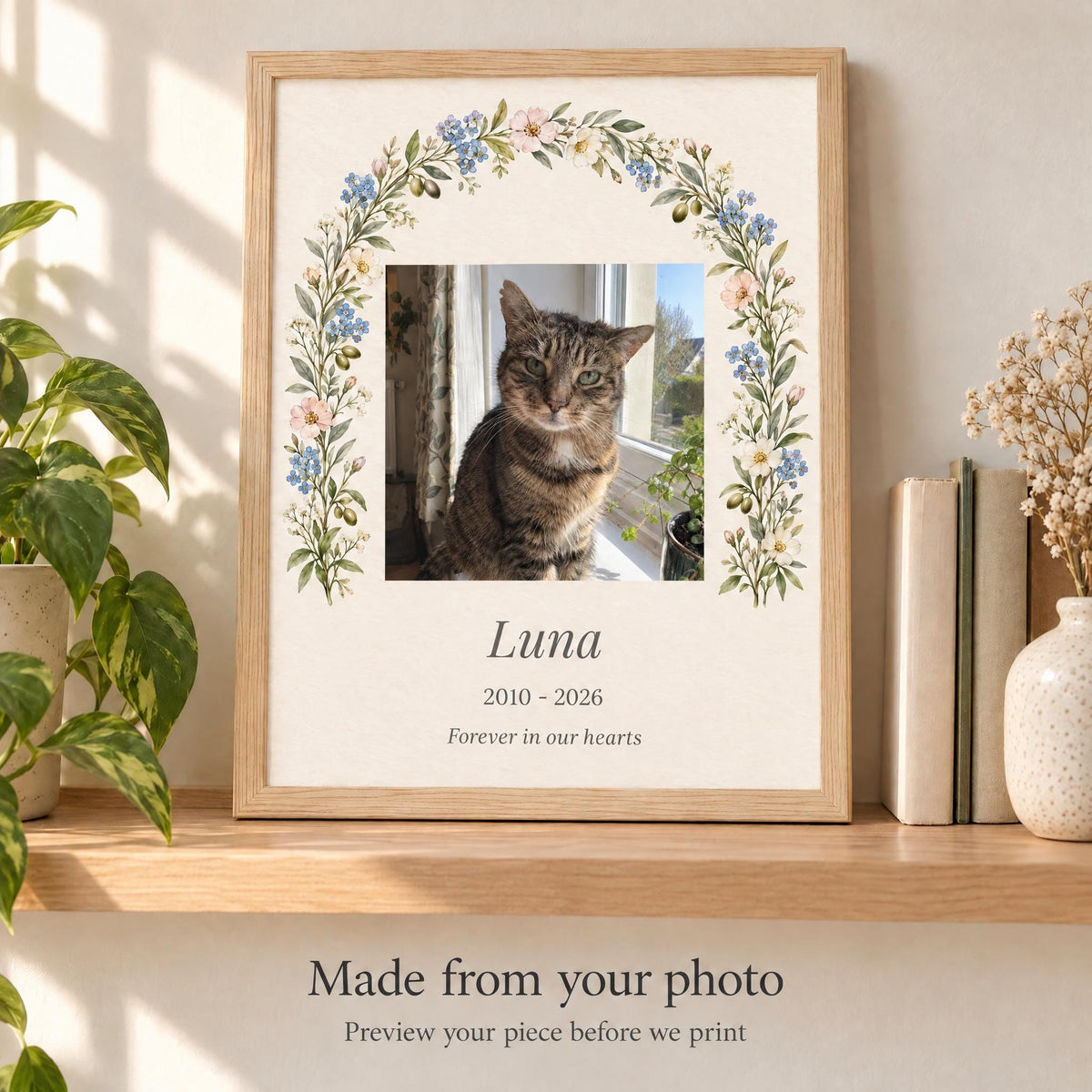 Custom cat memorial print with the cat's photo, name and years in a watercolor flower arch, framed on a sunny shelf