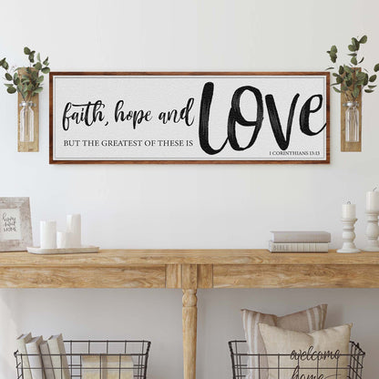 Long white canvas sign with a brown border and black brush lettering, faith, hope and LOVE, but the greatest of these is