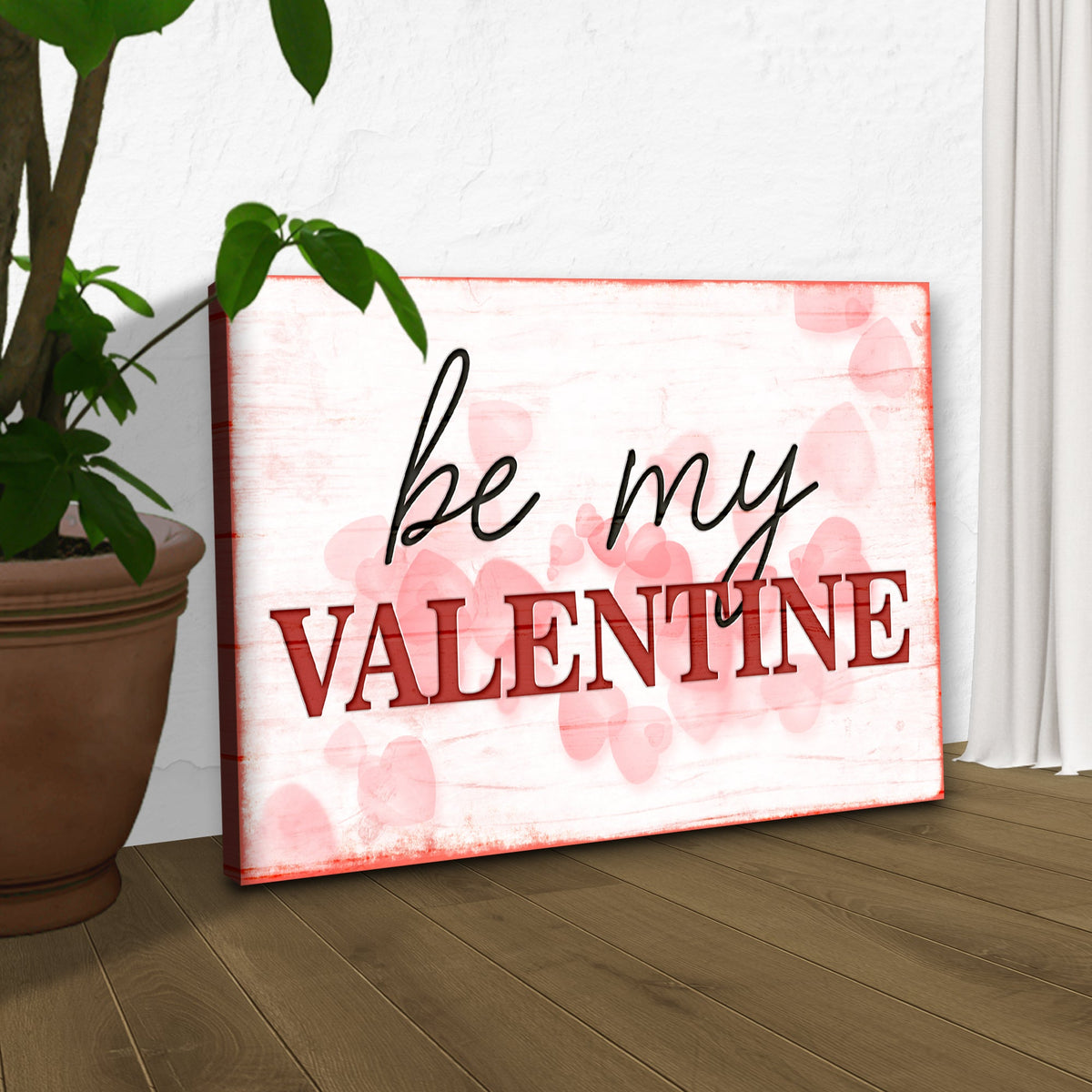 Be My Valentine canvas leaning beside a potted plant on a wood floor, angled view