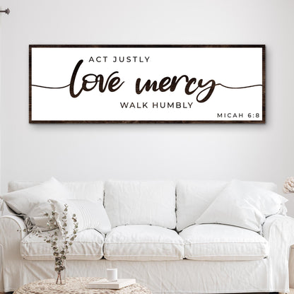 Long white canvas sign with a dark edge and bold brown brush script, love mercy, Micah 6:8, above a white sofa