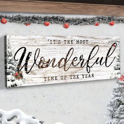 Angled close-up of the black script Wonderful Time of the Year canvas on a white wall under a tinsel garland