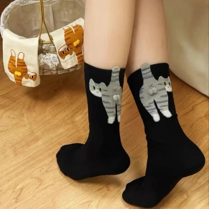 Black socks with cat designs worn by a person on a wooden floor.