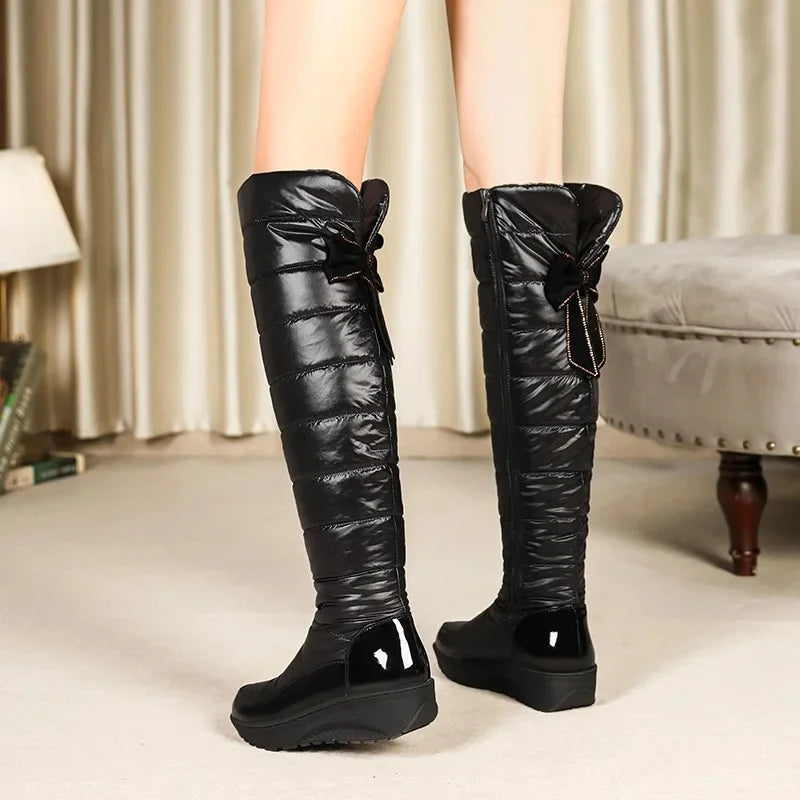 Black knee-high winter boots with bows worn indoors on a neutral background