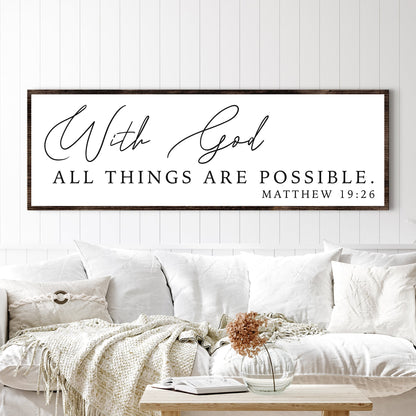 Long white canvas sign with fine black script, With God, and Matthew 19:26 above a white sofa with a knit throw