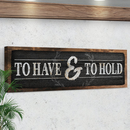 Angled close view of the long black wood-look sign with white capitals on a white wall under a wood shelf
