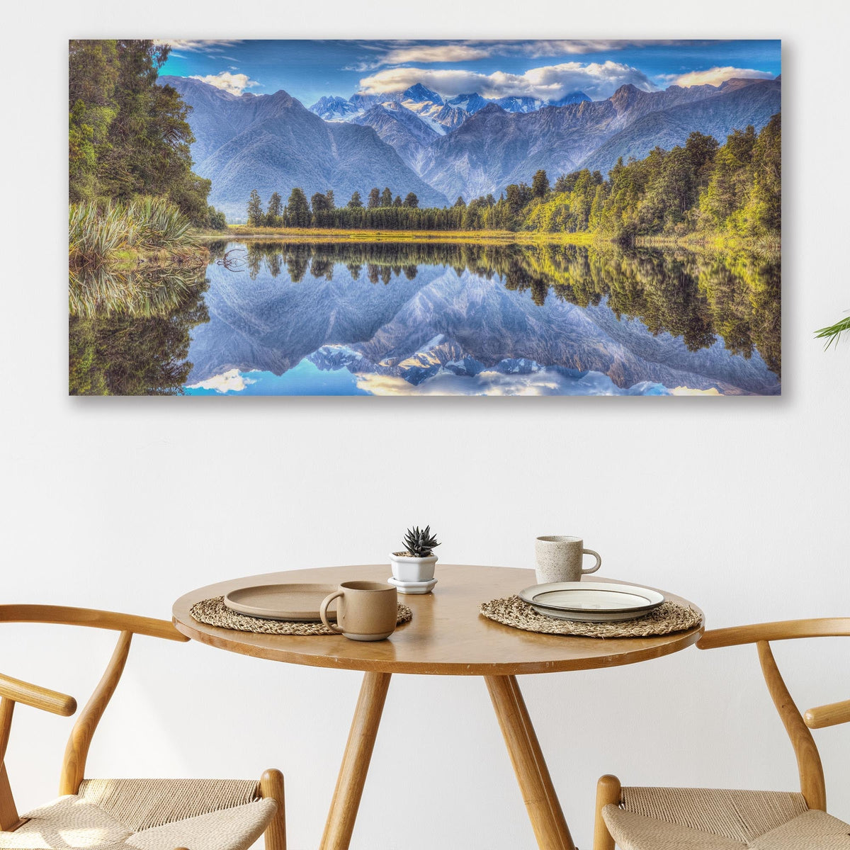Wide canvas of snowy mountains and forest mirrored in a still lake, above a round dining table