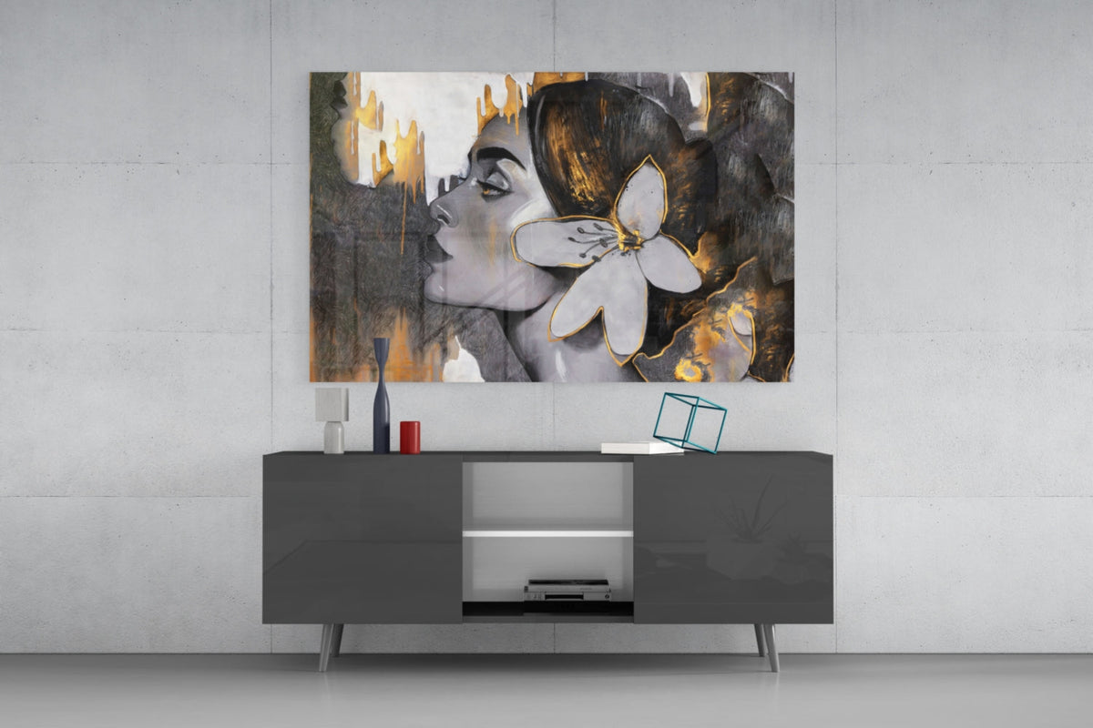 Woman with a white lily in gold and gray glass wall art above a gray sideboard with a red lamp on a concrete wall