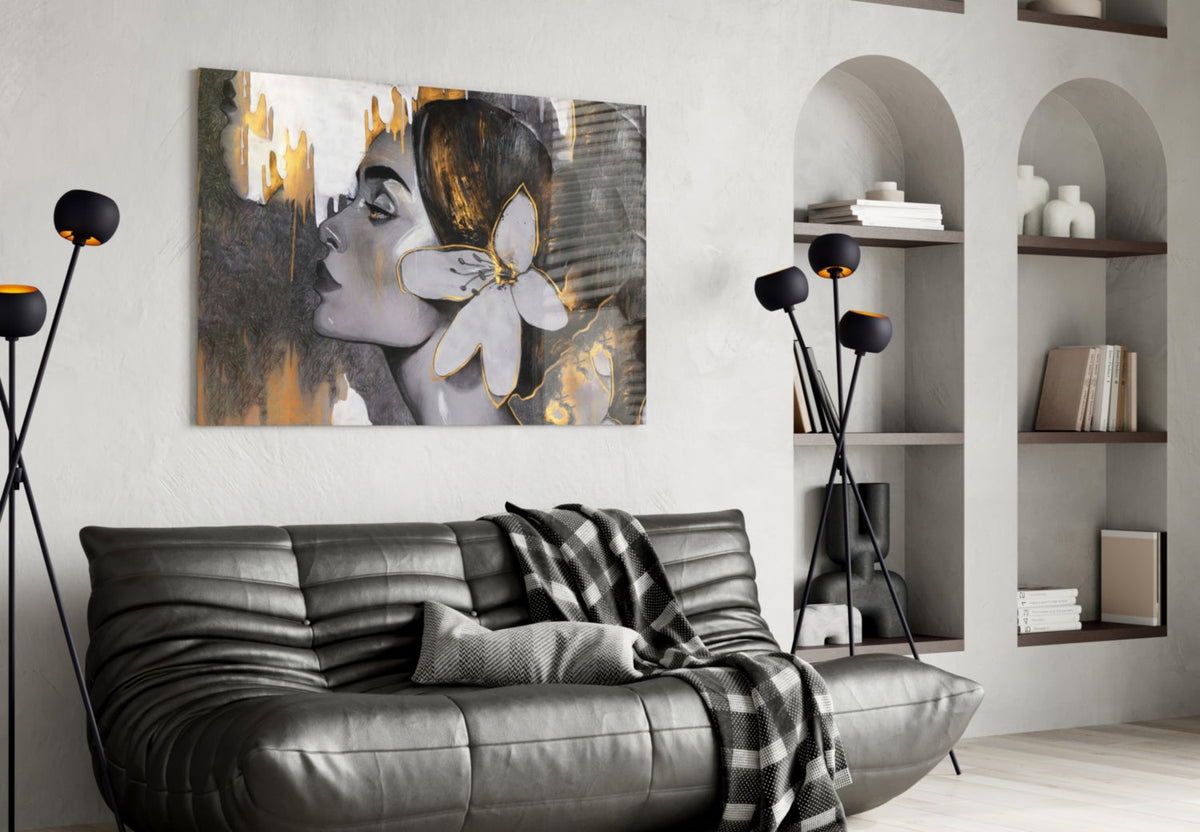 Woman with a white lily in gold and gray glass wall art above a black leather sofa beside arched shelves