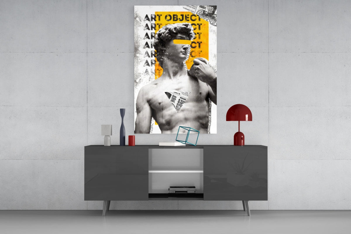 Marble statue on yellow newsprint collage glass wall art above a gray sideboard with a red table lamp on a concrete wall