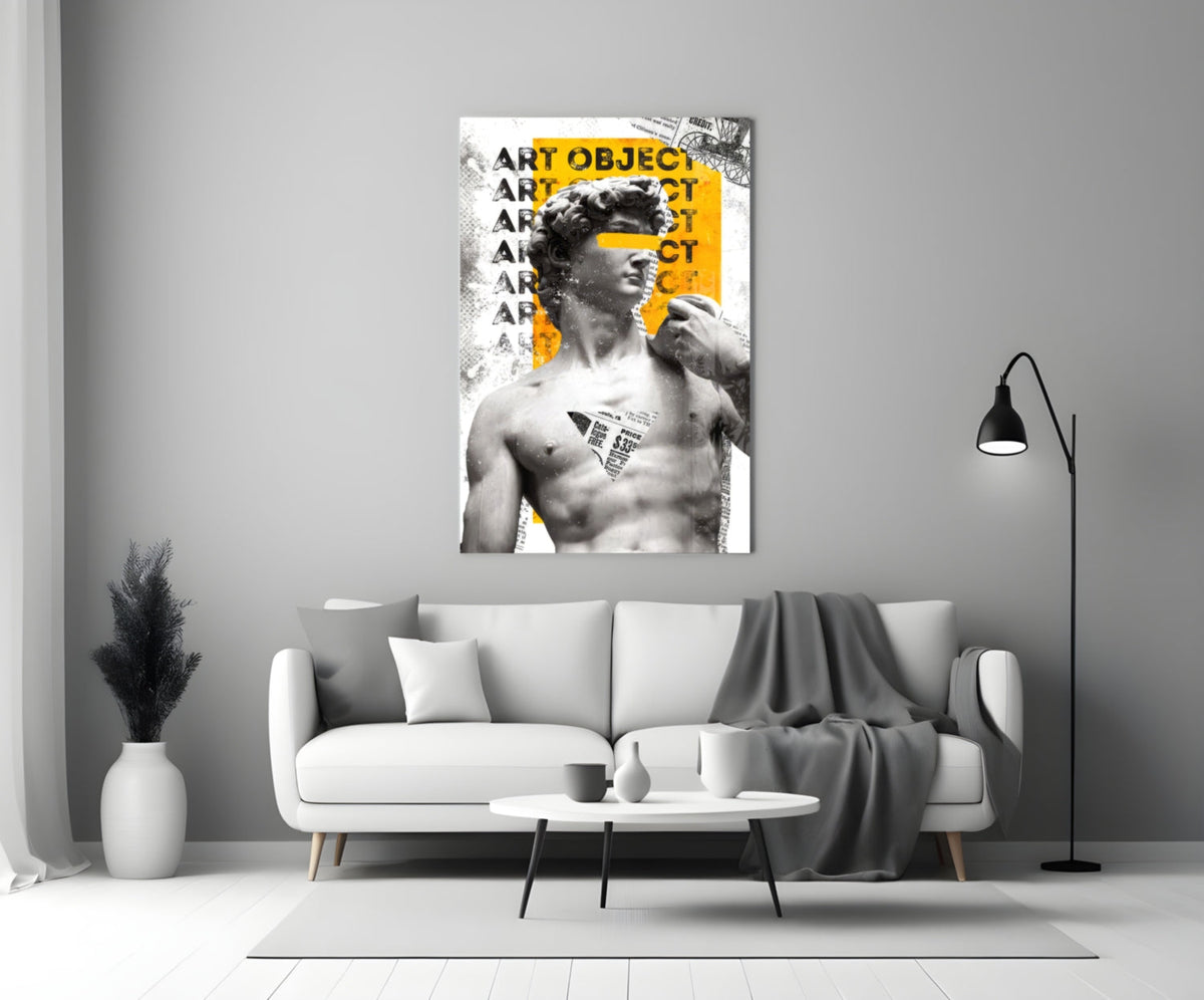 Marble statue on yellow newsprint collage glass wall art above a light gray sofa with a gray throw and a black floor lamp