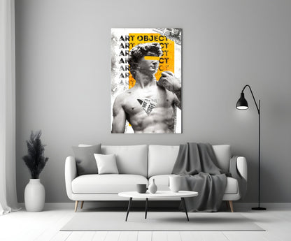 Marble statue on yellow newsprint collage glass wall art above a light gray sofa with a gray throw and a black floor lamp