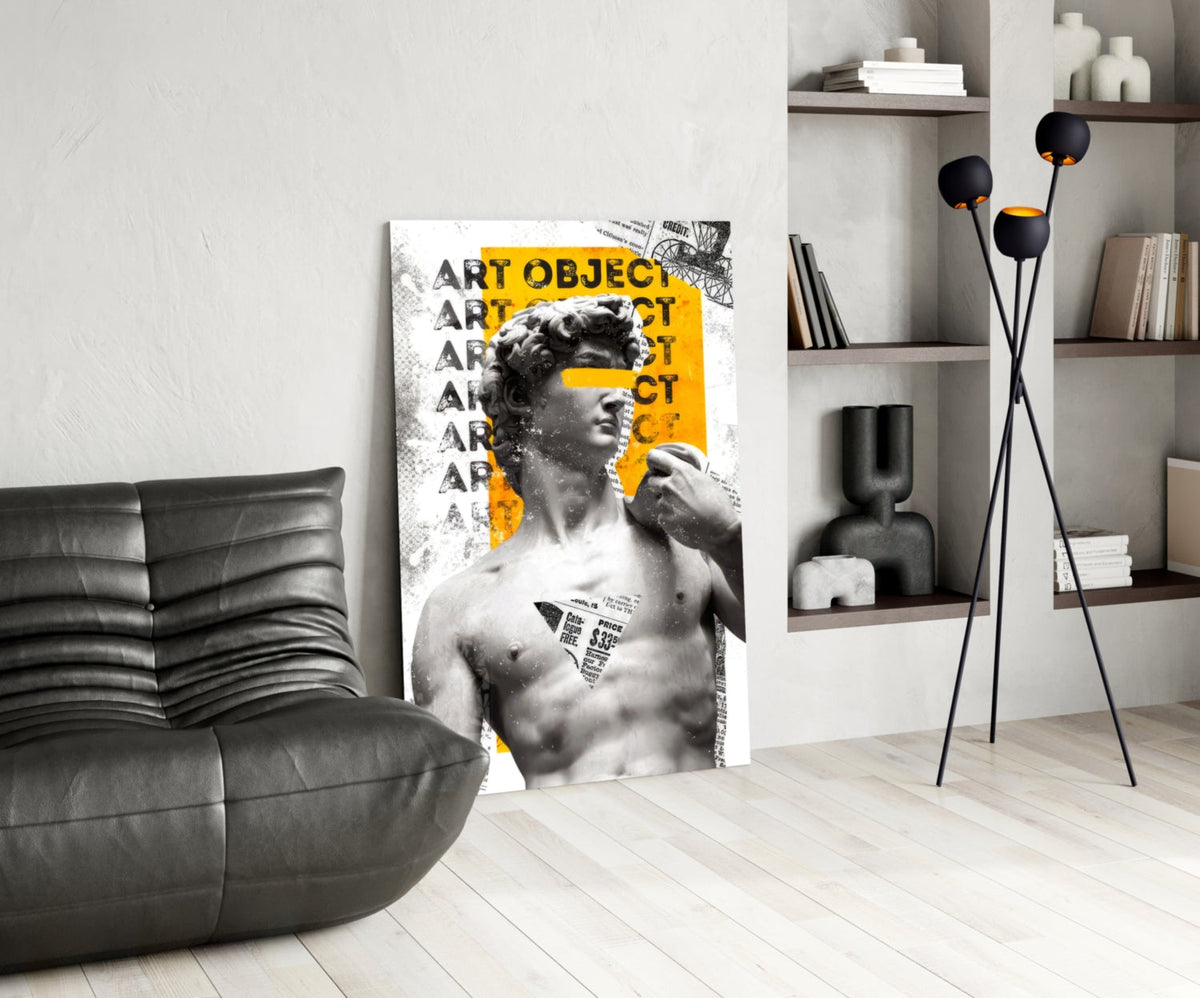 Marble statue on yellow newsprint collage glass wall art leaning beside a black leather lounge chair and open shelves