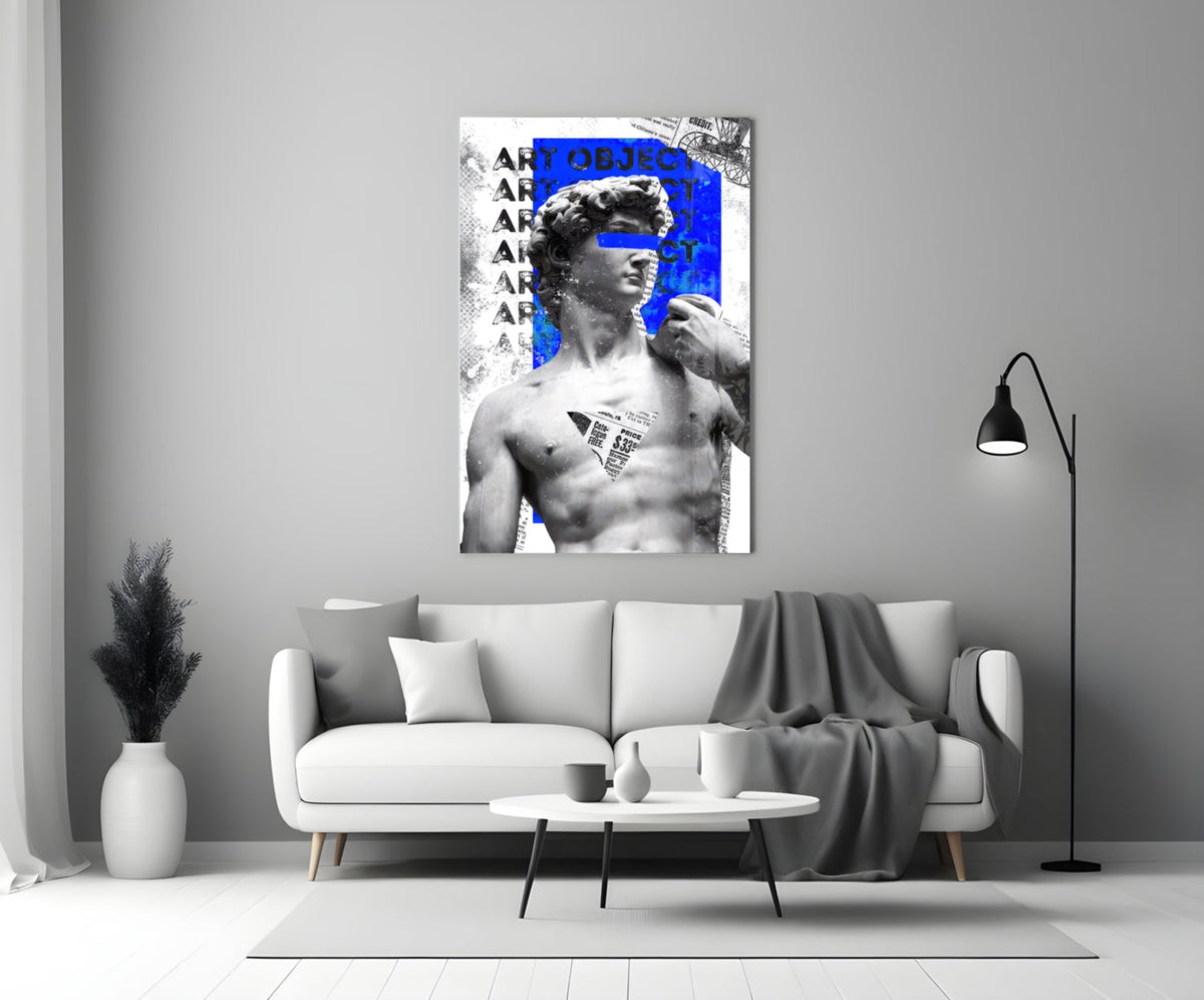 Marble statue on blue newsprint collage glass wall art above a light gray sofa with a gray throw and a black floor lamp